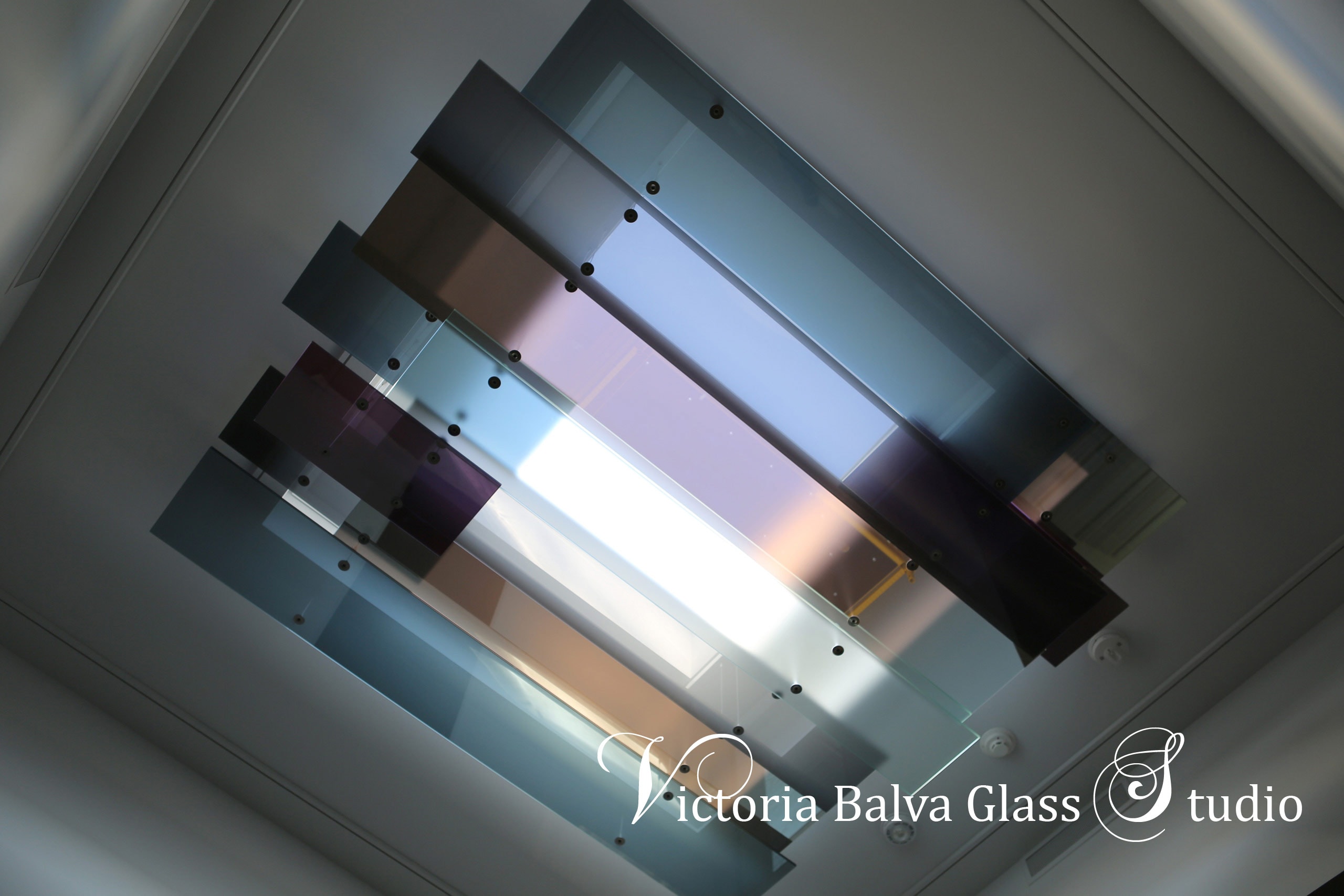 Contemporary art glass skylight installation in minimalistic style Laminated reflective textured colored glass with polished glass edge suspended on stainless steel hardware and steel cables for contemporary residence in Toronto